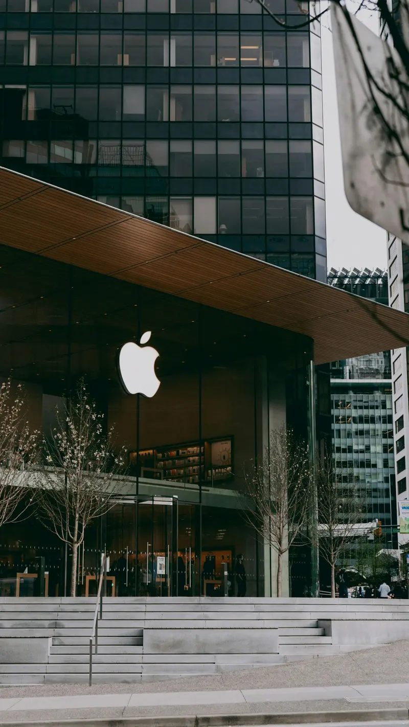 The glass storefront of an Apple Store, its lit logo glowing under a wood-panelled overhang.