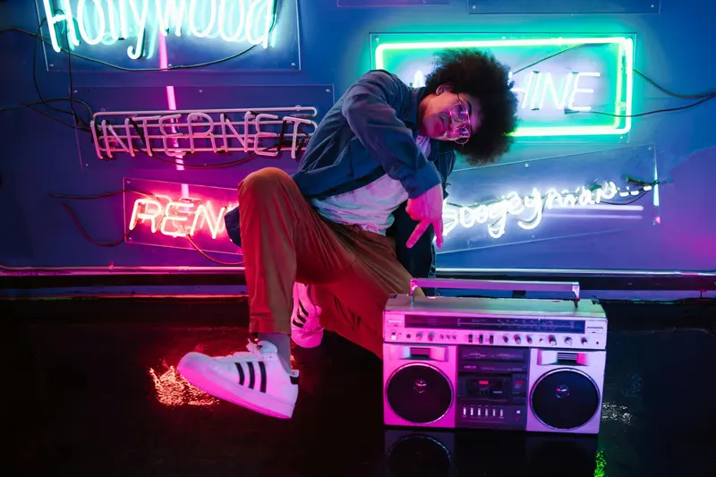 A person posing beside a vintage boombox in front of a wall of glowing neon signs.