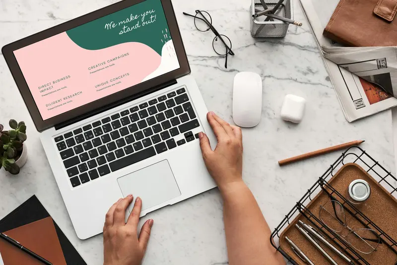An overhead shot of hands on a laptop showing a pastel brand presentation that reads 'We make you stand out'.