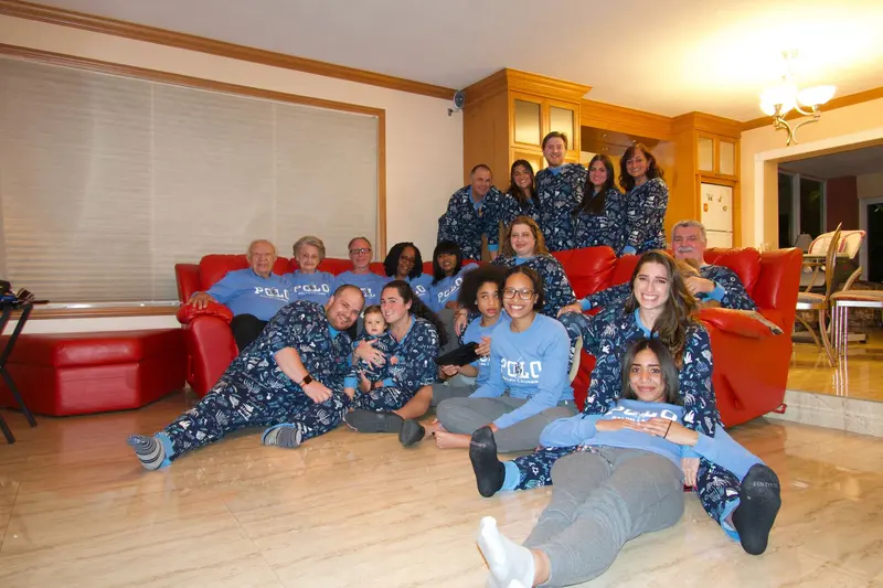 A large family in matching Chanukah pyjamas crowded onto and around a red sofa for a group photo.