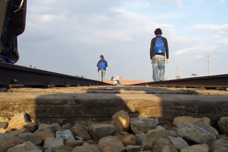 Visitors walking along the railway tracks at Auschwitz-Birkenau, the entrance building in the distance.