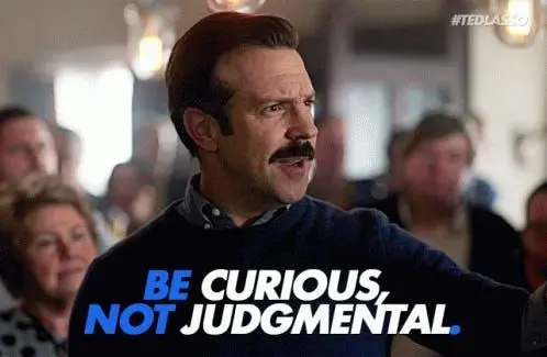 Ted Lasso mid-speech in a pub, captioned 'Be curious, not judgmental'.