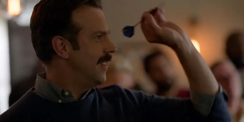 A man with a mustache is throwing a dart in the air.