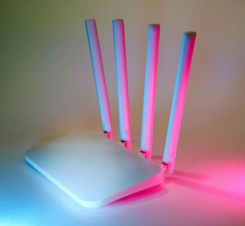 A white four-antenna Wi-Fi router lit by pink and blue studio light.