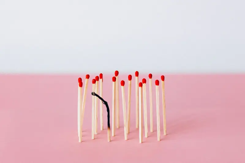 A bunch of matches are lined up in a row on a pink surface with one burnt-out.